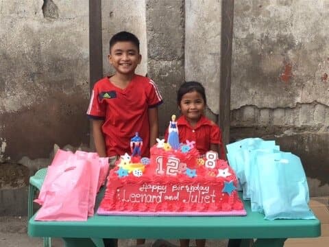 Two of the month's birthday children behind their cake, which says Happy Birthday Leonard and Juliet.