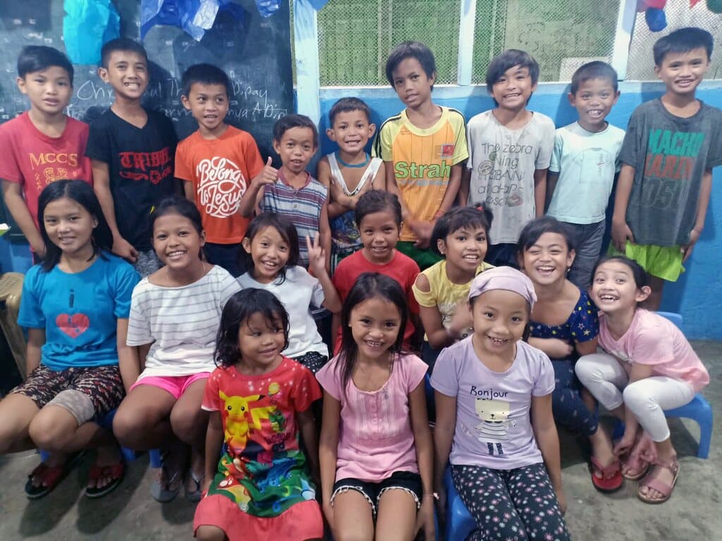 About twenty children in the classroom, squeezed together for a group photo and smiling.