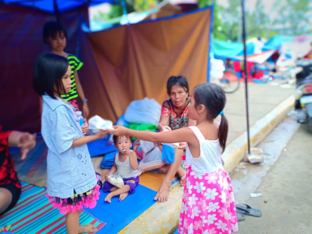 After the fire: a girl from Hay Nako hands a food parcel to a family sheltering under a tarp.